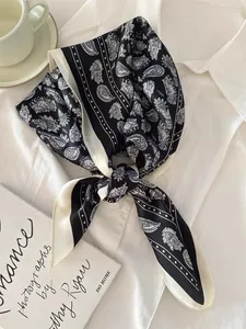 Close-up of a black and white paisley silk scarf styled on a crisp white shirt.