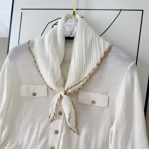 Detail showing the pleated texture and tan border of a white lightweight silk scarf