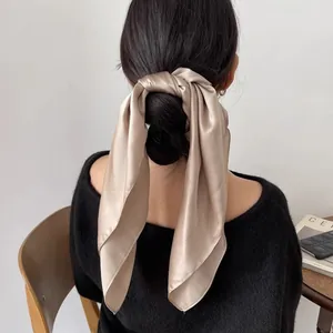 Élégant foulard en soie champagne noué comme accessoire sur un chignon.