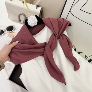 Detail view of a soft burgundy pleated square scarf styled on a white top.