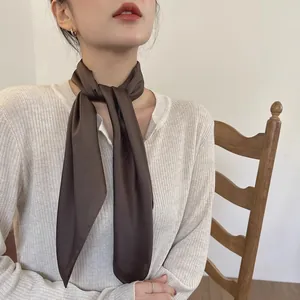 Vue détaillée d'une femme portant un élégant foulard en soie marron foncé avec un haut blanc.