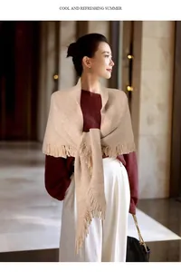 Elegante chal triangular de punto beige con borlas llevado por modelo en entorno interior