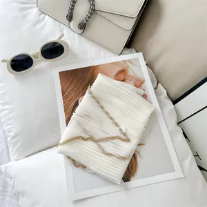 Detail shot of a lightweight white pleated silk scarf featuring elegant tan contrast piping.