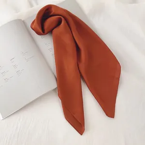 Détail d'un foulard en soie orange brûlé à la texture lisse présenté sur un magazine