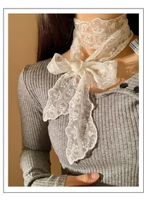 Detailopname van het delicate witte bloemenkantlint dat als elegante strik om de hals zit