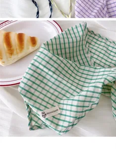 Dettaglio di un foulard triangolare a scacchi verdi con etichetta tessuta chic gufo.