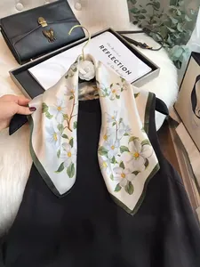 Close-up of elegant white silk scarf with floral print and green border on hanger.