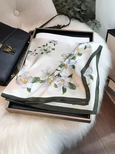 Detailed view of an elegant white floral silk scarf with green edges on a luxury gift box