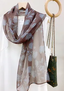 Close-up detail of an elegant brown floral chiffon long scarf draped over a white dress