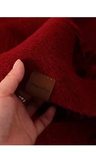 Detalle macro de la suave bufanda de punto roja con etiqueta de cuero decorativa