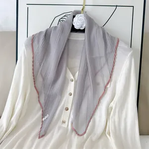 Detail of a grey pleated silk scarf with pink contrast trim draped over a white shirt.