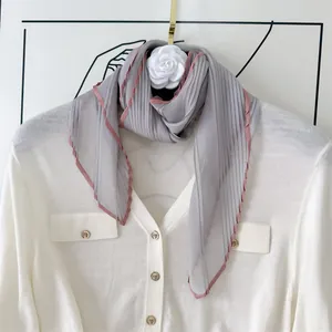 Close-up detail of a lightweight grey pleated scarf with elegant pink contrast borders