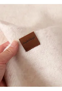 Primer plano de bufanda de punto crema con textura cepillada y etiqueta de cuero marrón