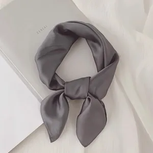 Détail d'un foulard en soie gris anthracite noué posé sur un fond très minimaliste.
