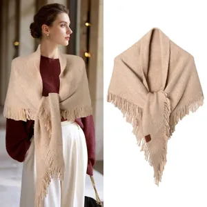 Vista detallada de un chal triangular de punto beige con flecos sobre una modelo