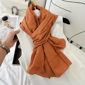 Detailed view of burnt orange crinkled cotton blend long scarf draped on white top