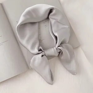 Vue détaillée d'un élégant foulard carré en soie satinée gris argenté sur un magazine ouvert.