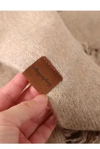 Primer plano de bufanda de punto beige que muestra la textura y la etiqueta de cuero.