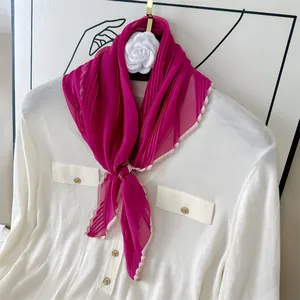 Detail view of a pleated fuchsia silk scarf with pink scalloped edges on a shirt.