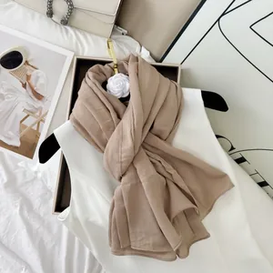Detailed view of a premium beige crinkled cotton blend scarf with white flower brooch