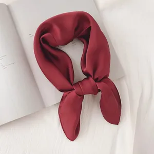 Détail d'un foulard en soie rouge vin uni noué sur un fond de tissu blanc texturé