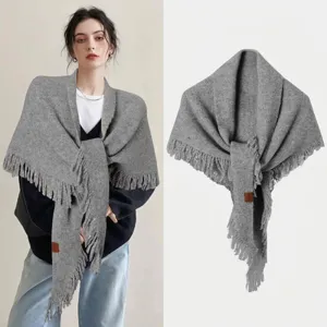 Vista detallada de un chal triangular de punto gris con flecos y pequeña etiqueta