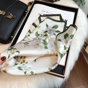 Elegant white silk square scarf with floral print and green border on magazine backdrop.