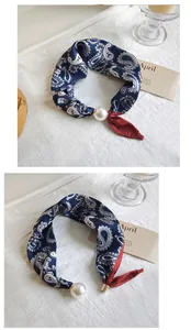 Detail view of navy paisley silk scarf featuring a large elegant pearl charm