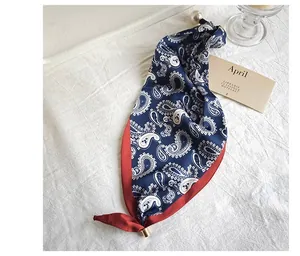 Elegant navy blue paisley silk scarf with red border and pearl detail on white fabric.
