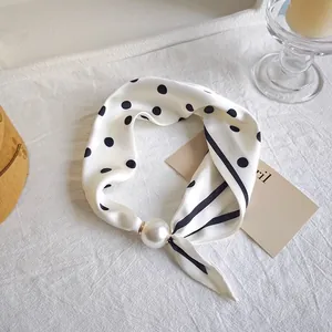 Detail view of a white silk scarf with black polka dots and a large pearl accessory.