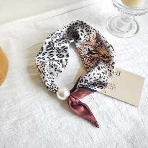 Close-up detail view of a leopard print silk scarf with a decorative pearl accessory.