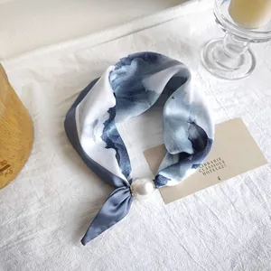 Close-up of a blue watercolor print silk scarf featuring an elegant pearl buckle