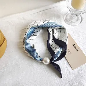 Detailed view of silk square scarf with geometric pattern and large pearl accessory