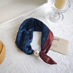 Elegant navy blue silk scarf with horse print and pearl ring accessory on a white fabric