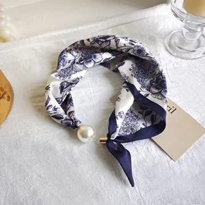 Detail view of a white and blue floral silk neckerchief with a decorative pearl pendant