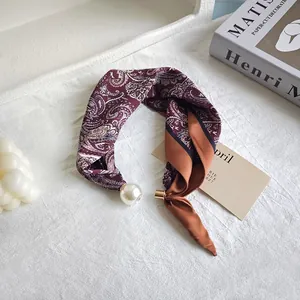 Close-up detail of burgundy paisley silk scarf with pearl fastener and gold clip