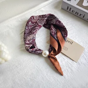 Detailed shot of an elegant paisley silk scarf featuring a large faux pearl embellishment
