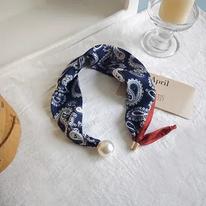 Close-up of navy blue paisley silk scarf with elegant pearl pendant detail.