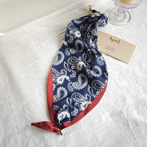 Macro view of navy paisley silk scarf with elegant red border and pearl ring detail