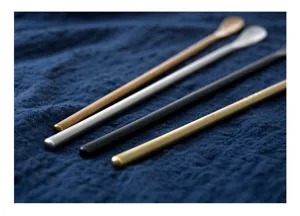 Close-up of four long-handled brushed stainless steel stirring spoons in various colors.