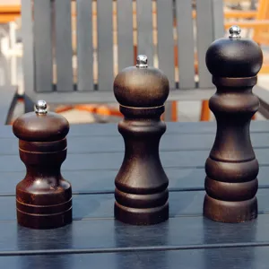 Set of three dark wooden manual pepper and salt grinders in different sizes on table