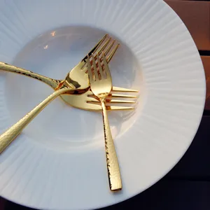 Creative gold hammered stainless steel forks set on a white plate.