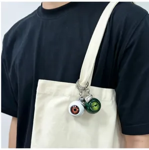 Detailed view of Gothic eyeball keychain charms hanging on a white canvas bag strap