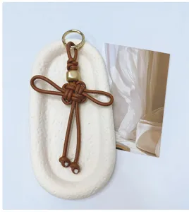 Porte-clés nœud chinois en cuir marron tissé à la main sur un plateau blanc texturé