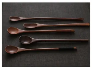 Detail view of five assorted long-handled vintage wooden stirring spoons on dark mat