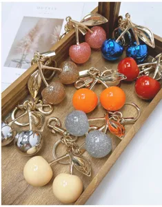 Detailed close-up showing various colorful glitter and glossy cherry keychains in a wooden tray