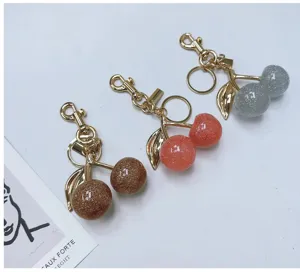 Close-up of three glittery cherry keychains in gold-tone metal with brown, pink and silver.