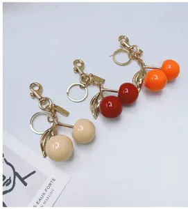 Adorable cherry bag charms in red, orange and beige with glossy golden hardware