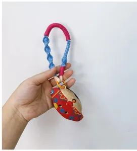 Close-up detail of a colorful handmade woven phone lanyard with a cute cartoon charm accessory