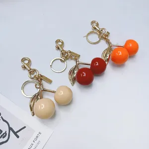 Realistic cherry bag charms in beige red and orange colors with glossy gold hardware